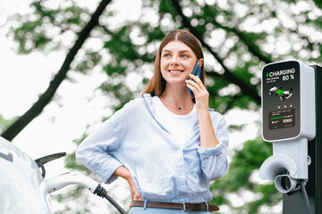 Young woman using smartphone online banking application to pay for electric car battery charging...