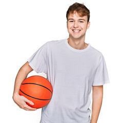 Obraz premium Young caucasian man holding basketball ball looking positive and happy standing and smiling with a confident smile showing teeth