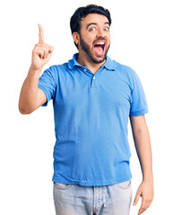 Young hispanic man wearing casual clothes pointing finger up with successful idea. exited and happy. number one.