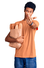 Young african american man holding paper bag with bread showing middle finger, impolite and rude...