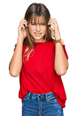 Obraz na płótnie Canvas Teenager caucasian girl wearing casual red t shirt covering ears with fingers with annoyed expression for the noise of loud music. deaf concept.