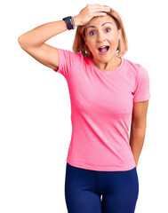 Young blonde woman wearing sportswear surprised with hand on head for mistake, remember error....