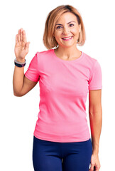 Young blonde woman wearing sportswear waiving saying hello happy and smiling, friendly welcome gesture