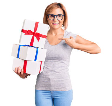 Young blonde woman wearing glasses holding gift pointing finger to one self smiling happy and proud