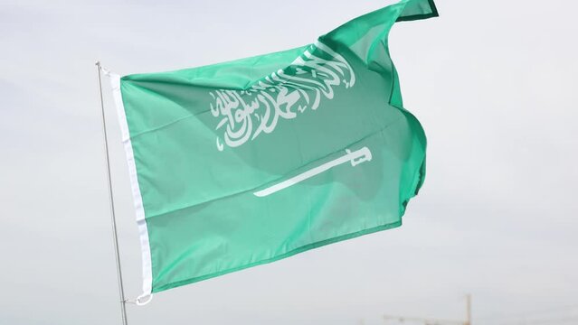 Flag of Saudi Arabia flutters in the wind against a blue sky background. 