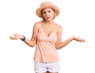 Young blonde woman wearing summer hat clueless and confused with open arms, no idea concept.