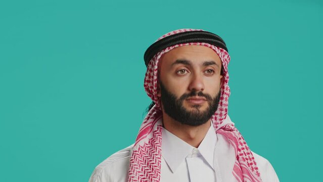 Person does three wise monkeys sign in studio, wearing islamic traditional attire and headscarf. Young adult covering his eyes, mouth and ears to create metaphor sign, concept.