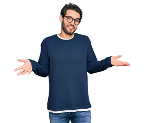 Young hispanic man wearing casual clothes and glasses clueless and confused expression with arms...
