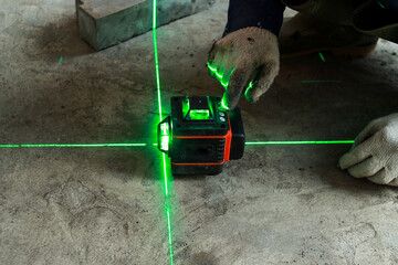 Worker wear glove and checks the floor level with a laser level meter on the cement walls in construction site. - obrazy, fototapety, plakaty