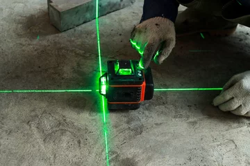 Fotobehang Worker wear glove and checks the floor level with a laser level meter on the cement walls in construction site. © Queenmoonlite Studio