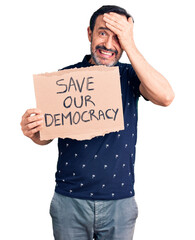 Middle age handsome man holding save our democracy cardboard banner stressed and frustrated with hand on head, surprised and angry face