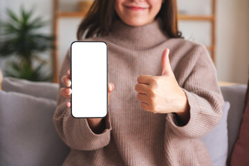Closeup image of a young woman making thumb up hand sign while holding and showing a mobile phone...