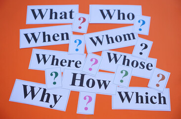 Paper cards with Wh-question words and question marks on orange background. Concept. Teaching aid. Education materials for teach WH- question. Asking questions. Suspicious symbol to find answer.      