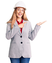 Beautiful young woman wearing architect hardhat amazed and smiling to the camera while presenting with hand and pointing with finger.