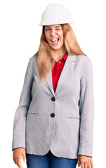 Beautiful young woman wearing architect hardhat winking looking at the camera with sexy expression, cheerful and happy face.