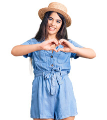 Brunette teenager girl wearing summer hat smiling in love doing heart symbol shape with hands. romantic concept.