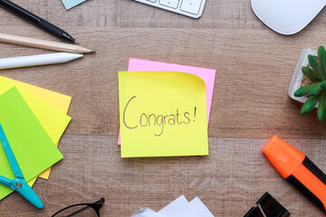 Congratulations text on sticky notes with office stationery over wooden background