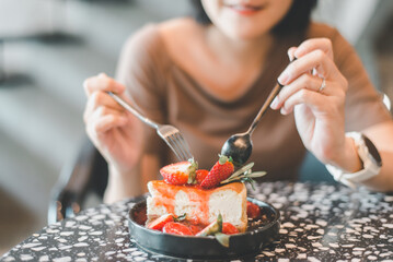 Happy woman eating delicious cake topping with fresh strawberry in a cafe