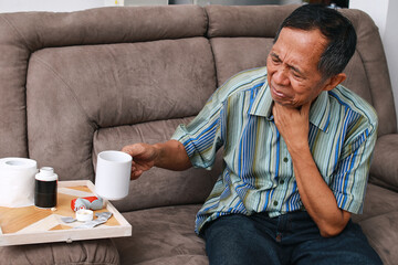Asian old man holding glass of hot water, suffering from a sore throat. 