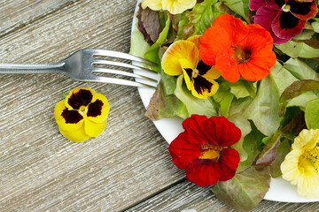 Plate of salad with edible flowers and lettuce on the wooden table.