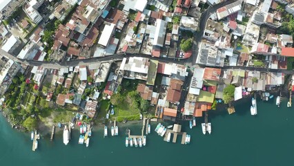 Drone top down descends on coastal village by Lake Atitlan Guatemala with boats docked at pier