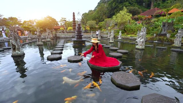 Female traveler feeds koi fish in Taman Tirtagangga Temple, Bali, Indonesia.	