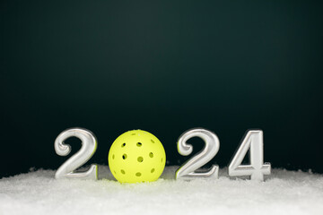 New year silver number 2024 sign on the snow with a yellow pickleball and dark teal background for...
