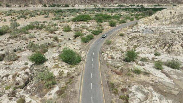 Aerial drone shot flying over a vehicle driving along the highway along the mountain foothills in Hingol, Balochistan, Pakistan on a rainy day. 
