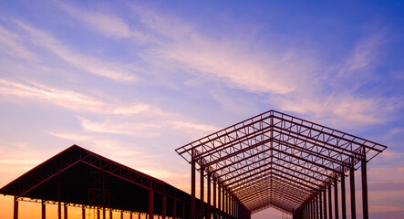Silhouette two metal industrial building outlines in construction site area against sunset sky...