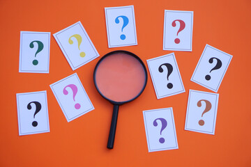 Paper cards of colorful question marks and magnifying glass on orange background. Concept. Teaching...