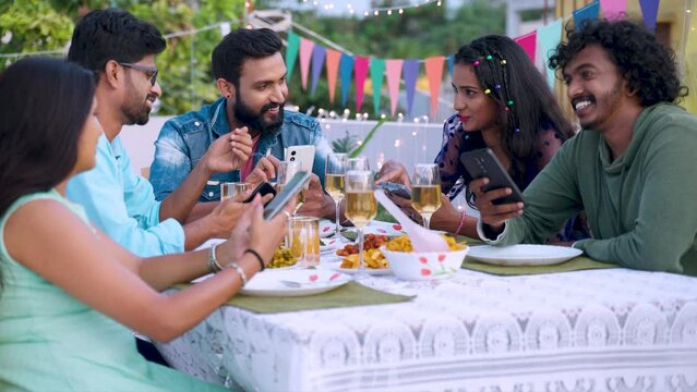 Group of friends spending time together with mobile phones during new year evening party celebration - concept of social media networking, influencers and birthday gathering.