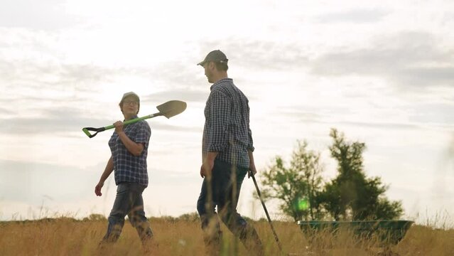 Farmers family with shovel and cart walks along harvested dry field after work