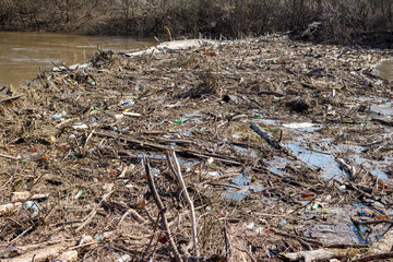 Pollution of the environment with non-degradable waste. A large garbage jam blocking the riverbed with a pile of dry branches and an accumulation of plastic waste