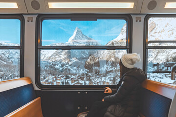 Happy Tourist woman looking out the window enjoying with the snow Matterhorn mountain while sitting...