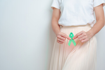 Woman holding Teal Ribbon on abdomen for January Cervical Cancer Awareness month. Uterus and Ovaries, Cervix, Endometriosis, Hysterectomy, Uterine fibroids, Reproductive and World cancer day concept - obrazy, fototapety, plakaty