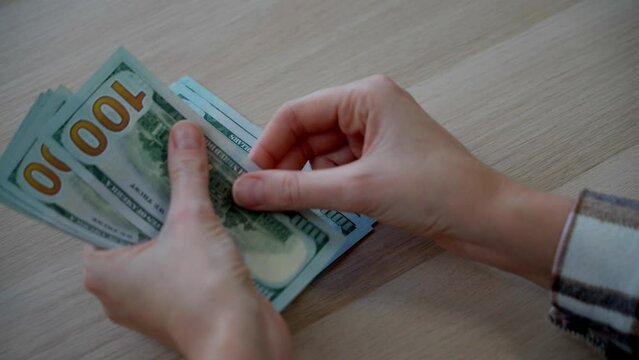 Close-up of a female's hands counting out hundred dollar bills onto the table. A woman calculates wages, taxes, utility bills or insurance premiums.