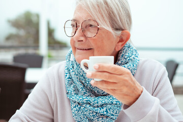 Portrait of attractive senior woman sitting at cafe table holding a cup of espresso coffee. Elderly...