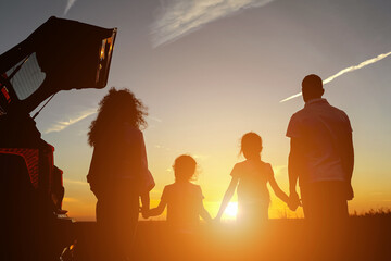 Family watches mesmerizing sunset holding hands in field near car. Concept of nature beauty and...