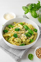 Vegetarian pasta with pesto sauce, broccoli, parmesan cheese and pine nuts on a white wooden...