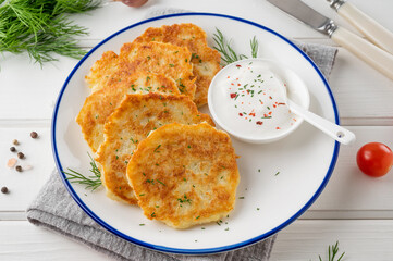 Potato pancakes, latkes or draniki with fresh herbs and sour cream on a plate on a white wooden background. Top view, copy space.
