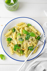 Vegetarian pasta with pesto sauce, broccoli, parmesan cheese and pine nuts on a white wooden background. Healthy food.