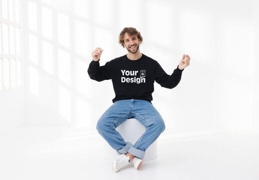 Mockup of man wearing customizable sweatshirt sitting on plinth in studio