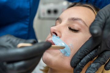 Young beautiful female client getting hot sugar wax epilation on upper lip of face in salon - obrazy, fototapety, plakaty