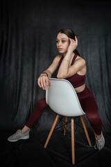 Athletic brunette young woman wear clort bra sitting on chair at studio shoot