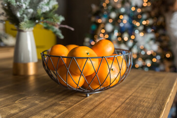 Fresh tangerines in Metal bowl on table against stylish decorated christmas tree with golden lights in scandinavian room. Atmospheric winter holidays at festive home.new year celebration