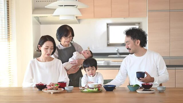 綺麗な家の食卓で食事をする赤ちゃんと祖母と子供のいる奇跡の幸せな同居家族 クローズアップの動画　 