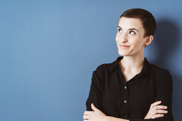 Amused Young Woman in Black Shirt Standing Against Blue Wall with Copy Space