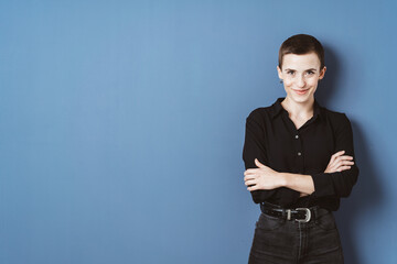 Confident Young Woman in Black Shirt Standing Against Blue Wall with Copy Space
