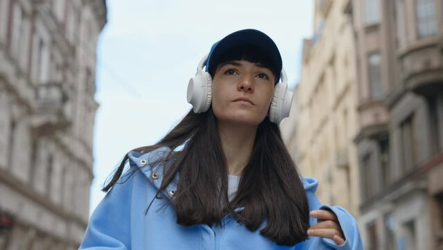 Cool Young Brown Woman in Wireless Headphones Dancing Outdoors in City Street, Having Fun Alone. Young Adult Happy Woman in Casual Clothes Dancing in Downtown