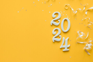 close up year of 2024 shape wood on yellow color background with white rolling ribbon and glitter...
